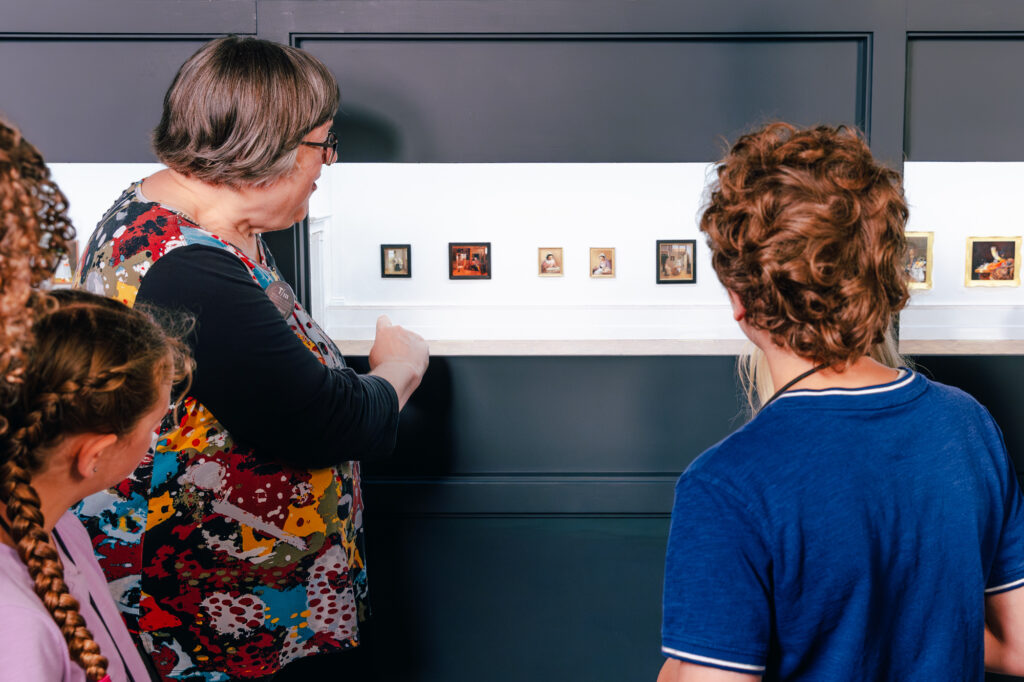 a museum staff member talks to students about the miniature paintings on display