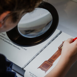 a child looks through a magnifying glass, using tweezers to move the hands on a miniature clock