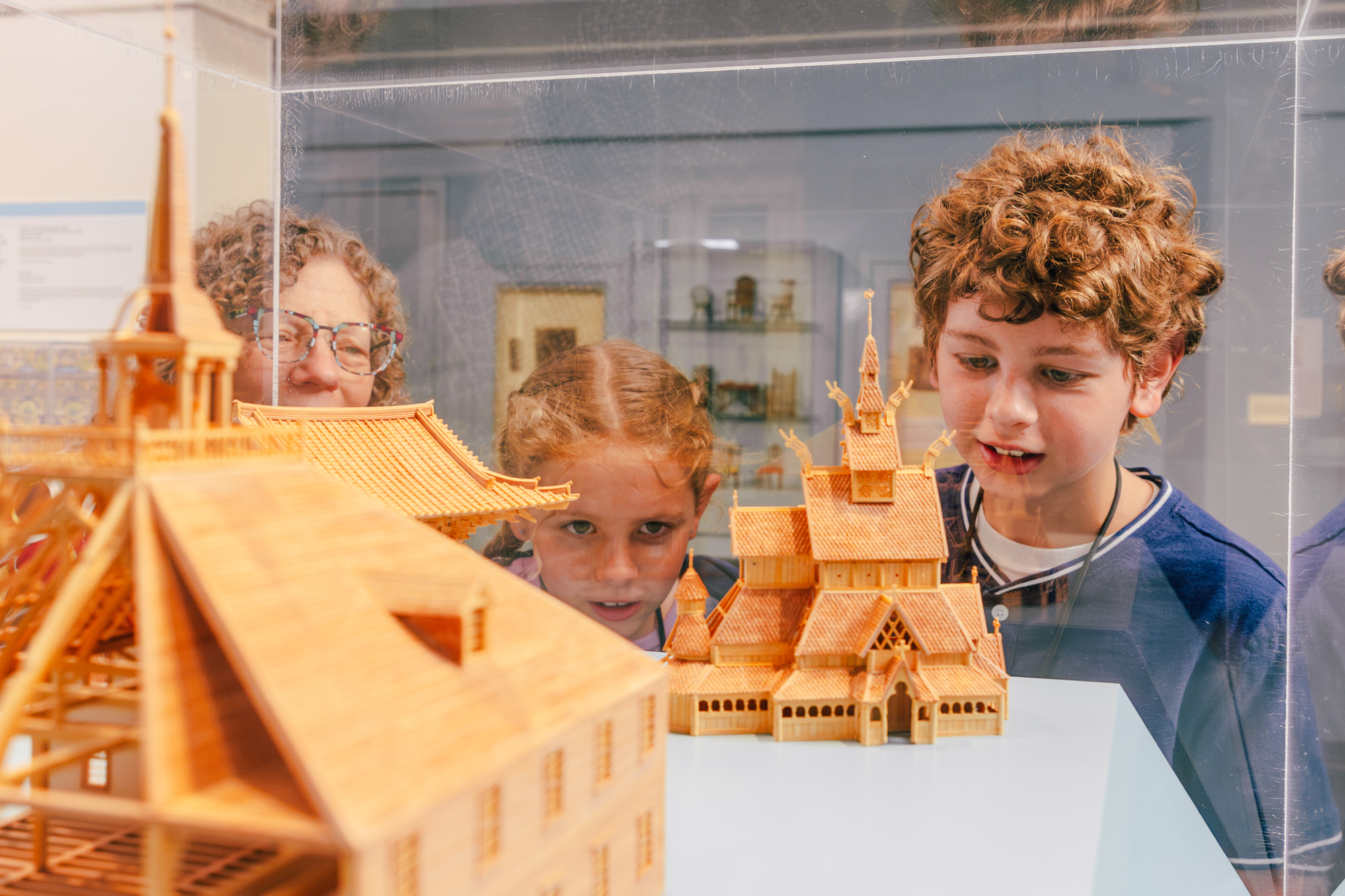 two children look at a miniature wooden church building with a museum staff memebr