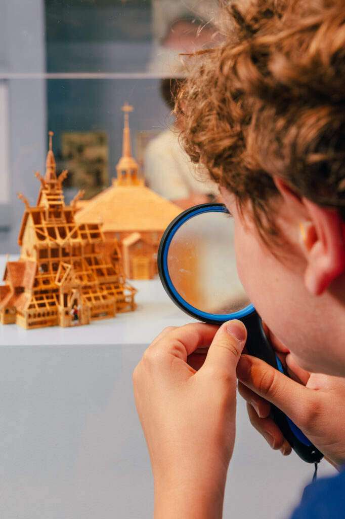 a young boy uses a magnifying glass to examine a small wooden church building