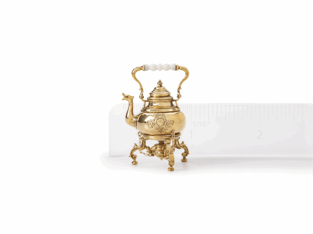 a miniature golden teapot next to a ruler show it is one inch wide