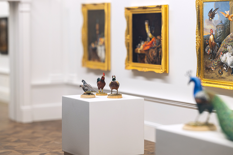 Close up photo of paintings and bird sculptures in the Miniature Art Museum exhibition.