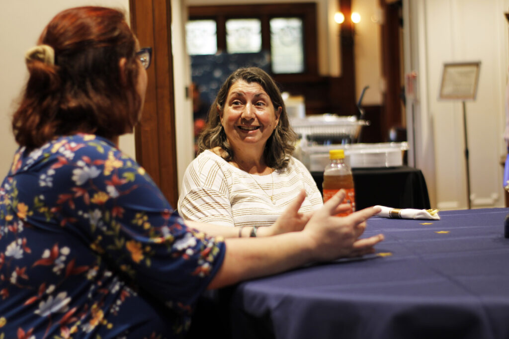 Two volunteers chatting and laughing at a table in the Tureman Mansion.