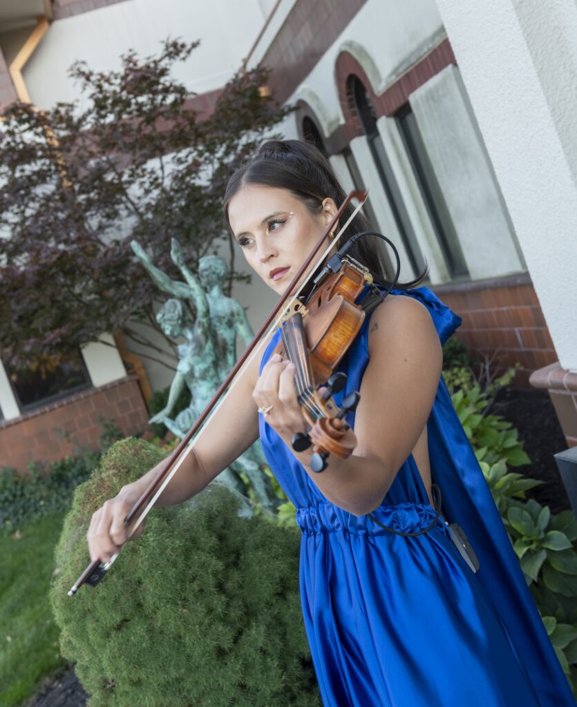 a woman in a vibrant blue dress playing a violin in a garden setting