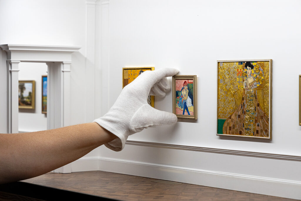 Curator's hand installing painting in the miniature art museum.