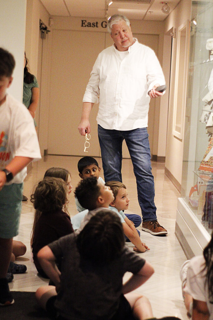 Teacher lecturing in front of a case to a group of kids.
