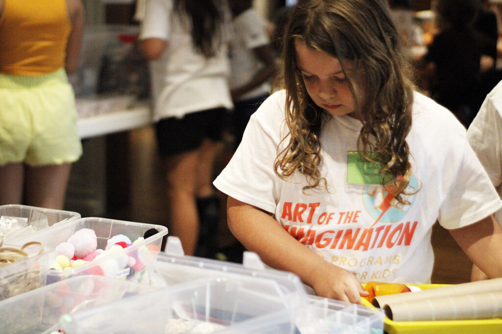 Young girl in a Summer Camp t-shirt picking out art supplies for a craft.