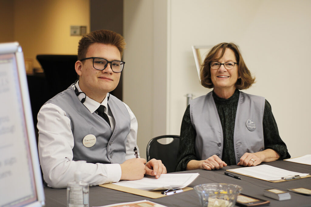 Two volunteers in grey vests working the check-in table.