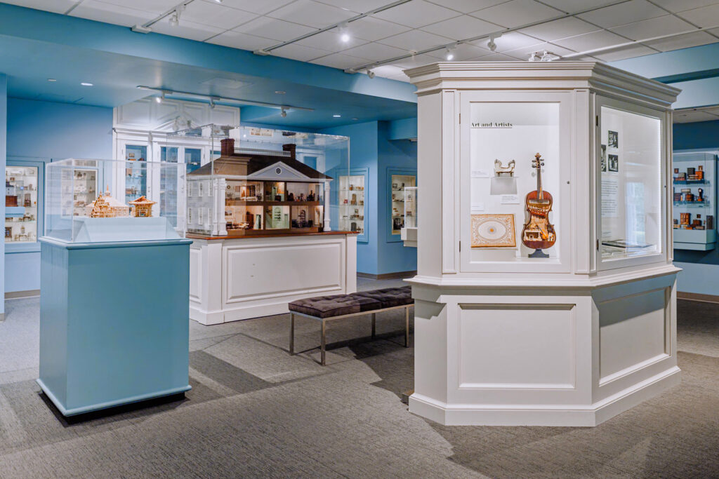 Miniature gallery showing a miniature violin and large house with miniature furniture inside.