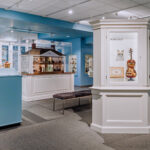Miniature gallery showing a miniature violin and large house with miniature furniture inside.